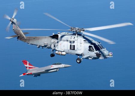Le Sikorsky MH-60R Seahawk, immatriculé N-977, est un hélicoptère maritime utilisé par la Royal Danish Air Force pour diverses opérations, y compris la guerre anti-sous-marine et les missions de recherche et de sauvetage. Il est vu ici aux côtés du F-16AM Fighting Falcon (E-601), un avion de chasse capable de jouer à la fois des rôles de défense aérienne et d'attaque au sol. Ensemble, ils représentent la polyvalence de la flotte de l'armée de l'air danoise. Banque D'Images