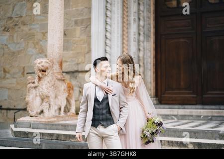 Mariée avec un bouquet de fleurs embrasse les épaules de marié souriant sur les marches à l'entrée de la basilique de Santa Maria Maggiore à Rome. Banque D'Images