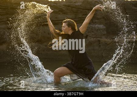 Femme d'âge moyen dansant et jetant de l'eau dans l'air, plage de Maioris, llucmajor, Majorque, Îles Baléares, Espagne, Europe Banque D'Images