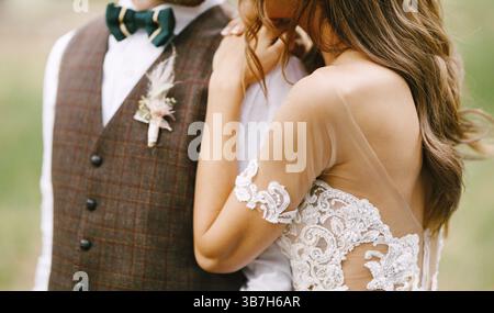 Belle mariée dans une robe brodée blanche embrasse l'épaule du marié. Portrait mi-longueur. Banque D'Images