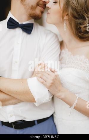 Le marié a plié ses bras sur sa poitrine, la mariée l'embrasse doucement par le coude et est sur le point de l'embrasser, gros plan. Banque D'Images