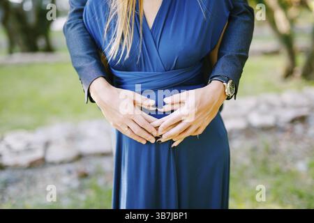 Mains de l'homme embrasse derrière le ventre enceinte de la femme dans une robe bleue. Banque D'Images