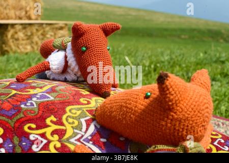 Deux jouets de renard en tricot doux, habillés de vêtements et avec des sacs à dos, blottis l'un à l'autre sur un tapis oriental coloré à côté d'un oreiller de jet, créant Banque D'Images