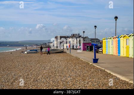 Une rangée de cabanes de plage colorées et des gens appréciant le soleil sur la promenade du front de mer de Seaford et la plage de galets dans l'East Sussex, en Angleterre. Banque D'Images