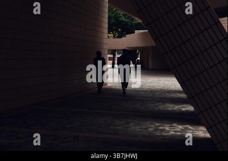 Deux silhouettes se promènent dans les couloirs ombragés du Centre culturel de Hong Kong Banque D'Images