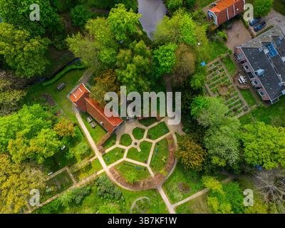 Vue aérienne d'un jardin verdoyant luxuriant avec des chemins symétriques, un bâtiment au toit rouge, des parcelles de légumes et des arbres environnants, créant un calme et un bien Banque D'Images
