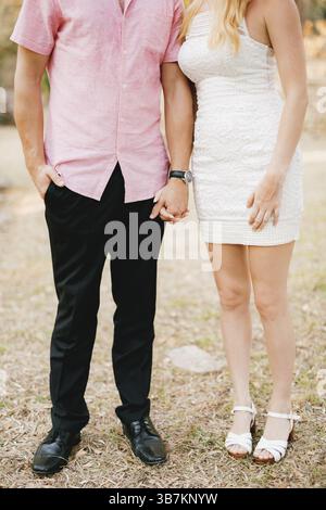 Un homme dans une chemise rose et une femme dans une robe blanche courte se tiennent côte à côte et tiennent tendrement la main . Banque D'Images