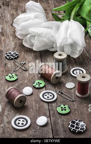 Ensemble d'accessoires de couture à partir de fils et de boutons sur le fond de tulipes blanches Banque D'Images