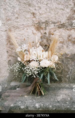 Le bouquet de mariée se tient près du mur d'un ancien bâtiment en pierre. Banque D'Images