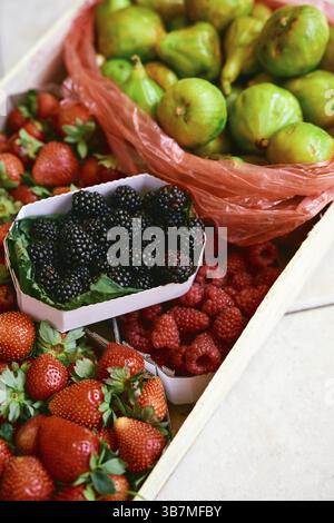 Caisse en bois avec des boîtes de fraises, framboises, figues et mûres se trouve sur une tuile. Banque D'Images