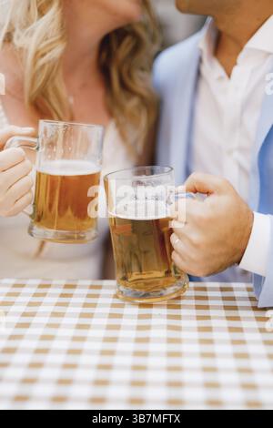 Un homme et une femme sont assis se serrant à table et tenant des tasses de bière dans leurs mains. Banque D'Images