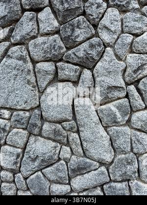 Mur en pierre grise rugueuse avec motif de maçonnerie irrégulier. Texture de roche naturelle utilisée dans les surfaces architecturales, pas de personnes, vue rapprochée. Banque D'Images