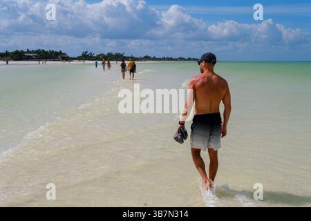 Holbox, Mexique - 10 février 2025 : un homme marche pieds nus le long du banc de sable sur le chemin du retour de Punta Mosquito, encadré par les eaux calmes et peu profondes Banque D'Images
