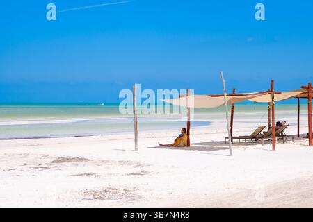 Holbox, Mexique – 10 février 2025 : une femme s’assoit tranquillement sous une simple canopée de plage, profitant de la vue paisible sur la mer turquoise et le sable blanc. Banque D'Images