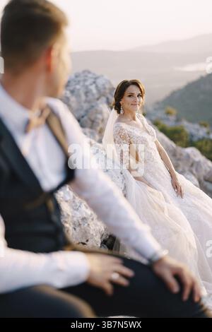 Un couple de mariage au sommet d'une montagne dans la baie de Kotor, la mariée sourit au marié au coucher du soleil. Photo de mariage de destination fine-art au Monténégro, Banque D'Images