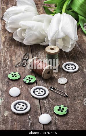 Ensemble d'accessoires de couture à partir de fils et de boutons sur le fond de tulipes blanches Banque D'Images