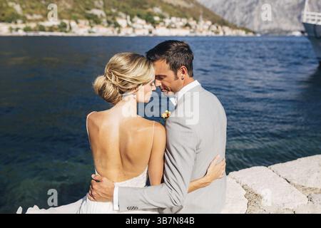 La mariée et le marié sont assis embrassant sur la jetée dans la baie de Kotor, en face d'eux est la vieille ville, en gros plan. Banque D'Images