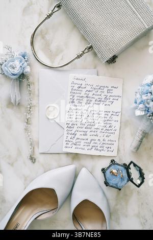 Vœu de mariage se trouve sur une enveloppe à côté des chaussures de mariée et sac à main sur une table en marbre. Banque D'Images
