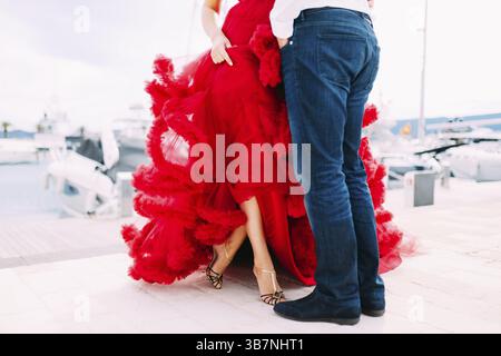 Homme debout devant une femme vêtue d'une robe rouge sur un quai de bateau au Monténégro. Banque D'Images
