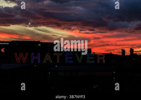 les lettres colorées du néon, quel que soit le signe, se détachent sur l'horizon noir d'auckland sous les nuages rouges du coucher du soleil Banque D'Images