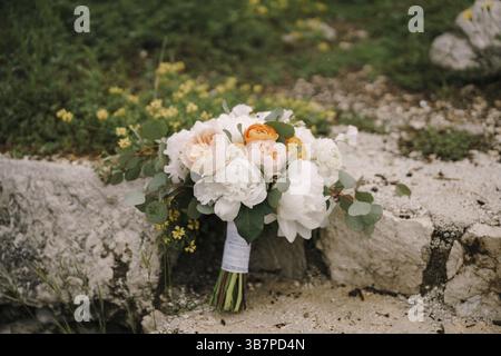 Bouquet de mariée de pivoines blanches, roses crème, papillons oranges et branches d'eucalyptus sur une passerelle en pierre. Banque D'Images