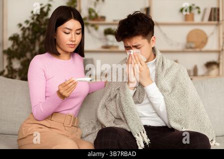 Petite amie qui traite un Boyfriend malade qui donne un médicament assis sur un canapé à l'intérieur Banque D'Images