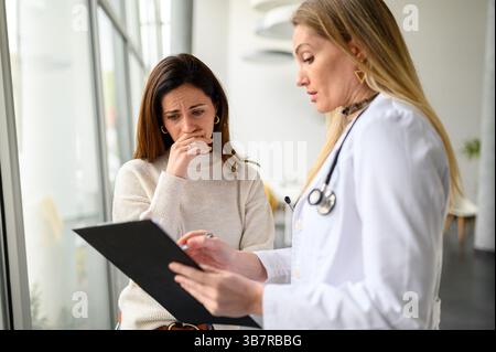 Médecin féminin expliquant les résultats des tests et guidant une jeune femme inquiète en clinique pendant la consultation Banque D'Images