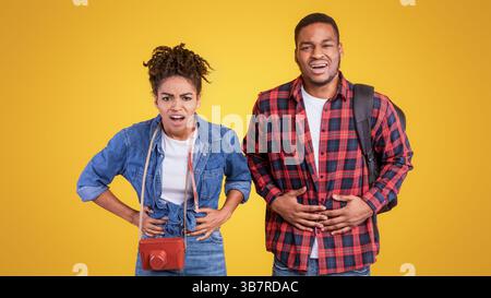Couple de voyageurs noirs ayant un stomachache se tenant au-dessus de Yellow Studio Background Banque D'Images