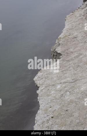 La vue aérienne nette met en valeur le contraste frappant entre une falaise blanche rocheuse, surélevée et dentelée et l'eau sombre, immobile et trouble qu'elle surplombe O. Banque D'Images