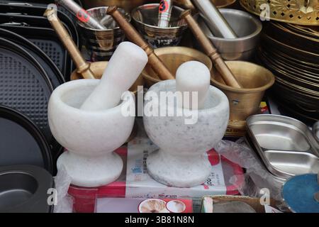 Une image en gros plan présente deux mortiers en marbre blanc bien en vue à côté de bols en laiton et un assortiment d'autres accessoires de cuisine Banque D'Images