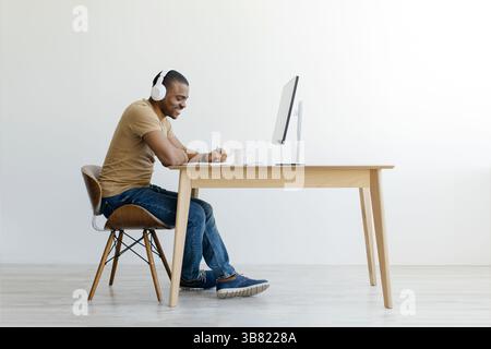 Souriant Noir Millennial Man dans les écouteurs étudier avec l'ordinateur à la maison Banque D'Images