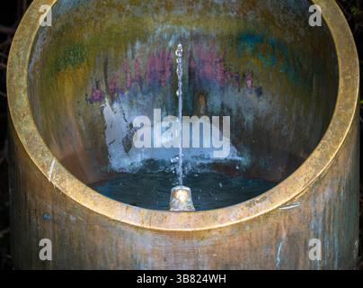 Une vue rapprochée d'une fontaine circulaire en pierre avec de l'eau qui coule du centre. La fontaine a une surface texturée altérée avec des notes de vert an Banque D'Images