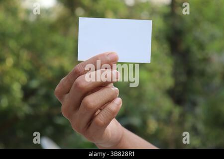 Gros plan capture la main d'une personne tenant une petite carte blanche rectangulaire, présentant une surface vierge parfaite pour afficher des informations, posée contre elle Banque D'Images