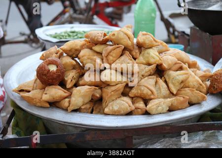 Un gros plan présente des samosas triangulaires dorés-bruns fraîches et un bonbon en forme de sphère reposant sur un plateau d'argent chez un vendeur en plein air dans la rue. Banque D'Images