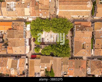 Vue aérienne de dessus d'une place historique bordée d'arbres entourée de vieux toits en tuiles dans la ville fortifiée médiévale d'Aigues-Mortes, France Banque D'Images