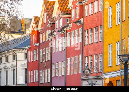 Des maisons peintes de couleurs vives bordent les rues de Copenhague, affichant des teintes vives de rouge et de jaune. Les visiteurs se promènent, profitant de la charmante architecture par une journée ensoleillée. Banque D'Images