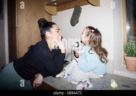 Femme souriante appuyée sur le comptoir de la cuisine et jouant avec sa fille à la maison Banque D'Images