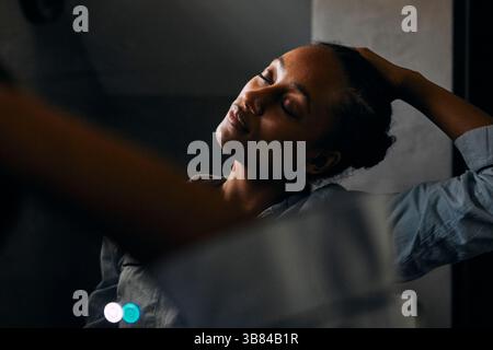Femme étirant le cou après s'être réveillé tout en se tenant devant le miroir à la salle de bain Banque D'Images