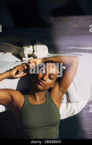 Femme avec les yeux fermés s'étirant tout en étant assis près du lit dans la chambre Banque D'Images