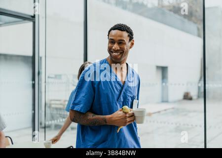 Heureux travailleur de santé masculin tenant une tasse de café et une banane regardant loin Banque D'Images