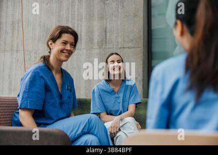 Des travailleuses de la santé souriantes qui passent du temps libre à parler entre elles dans un bâtiment hospitalier Banque D'Images