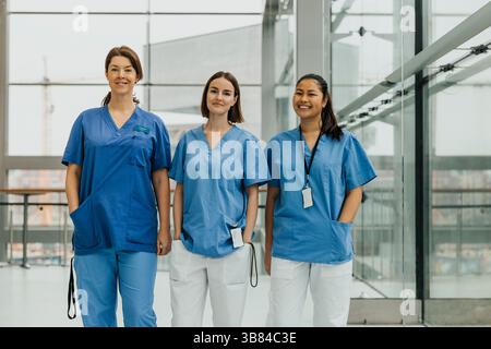 Portrait de professionnelles médicales féminines souriantes debout côte à côte avec la main dans la poche dans le couloir de l'hôpital Banque D'Images