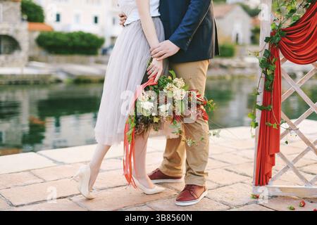 L'homme embrasse la femme avec un bouquet de fleurs dans ses mains tout en se tenant sur la jetée près d'un écran décoratif sur fond de vieilles maisons. Banque D'Images