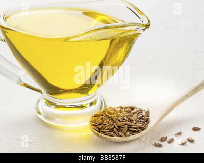 Graines de lin brunes dans une cuillère et huile de lin dans une cruche en verre sur fond de béton blanc texturé tendance. L’huile de lin est riche en acides gras oméga-3 Banque D'Images