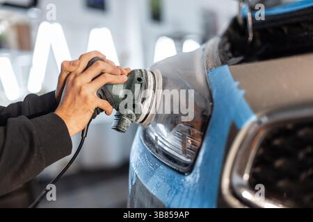Homme professionnel polissant phare de voiture dans le centre de détail. Entretien de la voiture Banque D'Images
