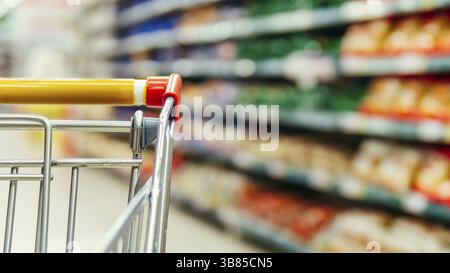 Panier au supermarché. Partie du chariot dans l'allée du supermarché. Étagères floues dans l'épicerie et le chariot. Copier l'espace pour le texte ou les dési Banque D'Images