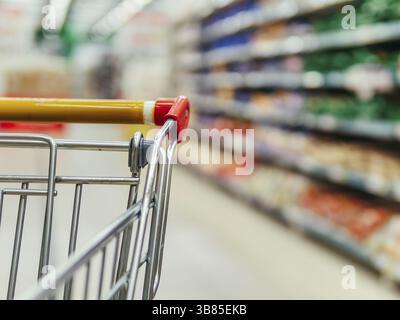 Panier au supermarché. Partie du chariot dans l'allée du supermarché. Étagères floues dans l'épicerie et le chariot. Copier l'espace pour le texte ou les dési Banque D'Images