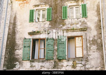 Ancien bâtiment de plusieurs étages avec fenêtres et volets en bois à la peinture pelée. Banque D'Images