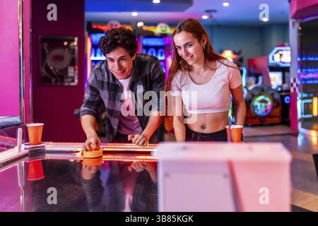 Jeunes amis multiethniques profitant d'un week-end ensemble en jouant au hockey pneumatique dans une salle de jeux Banque D'Images