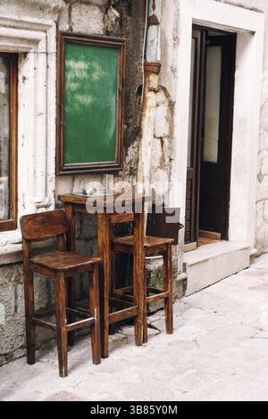 Table haute en bois et deux chaises près du mur d'un petit bar dans la rue. Banque D'Images